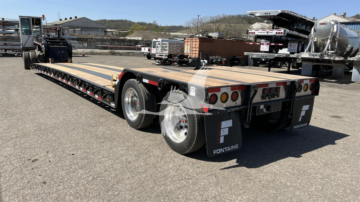 Fontaine XN20 lowboy trailer showing long flatbed with dual rear axles and loading ramps, Fontaine branding on mud flaps, in an outdoor lot