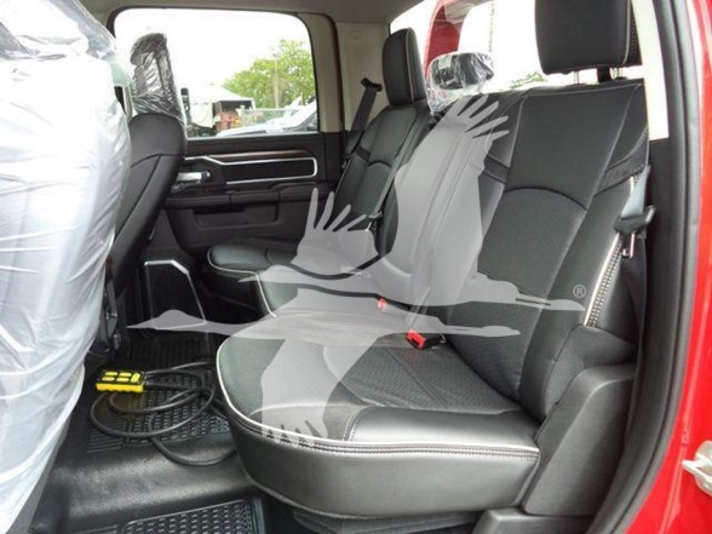 Ram 2024 Laramie cabin interior showing rear bench seat in black fabric with light stitching, door panel, seat belts, and protective plastic on front seat visible.
