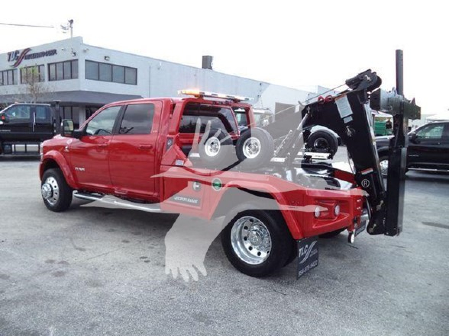Tow truck with a Ram pickup cab connected to a large wheel-lift tow arm. Visible text on the vehicle includes logos and brand graphics on the door and sides.