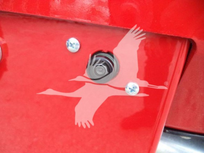 Vehicle rear showing hitch receiver with decal of flying bird on red surface. Bolt heads and a circular connector or hitch mount visible.