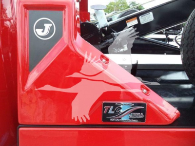 Ram pickup truck tailgate with TLC logo and J logo badge, red paint, partial view of black tonneau area and winch equipment