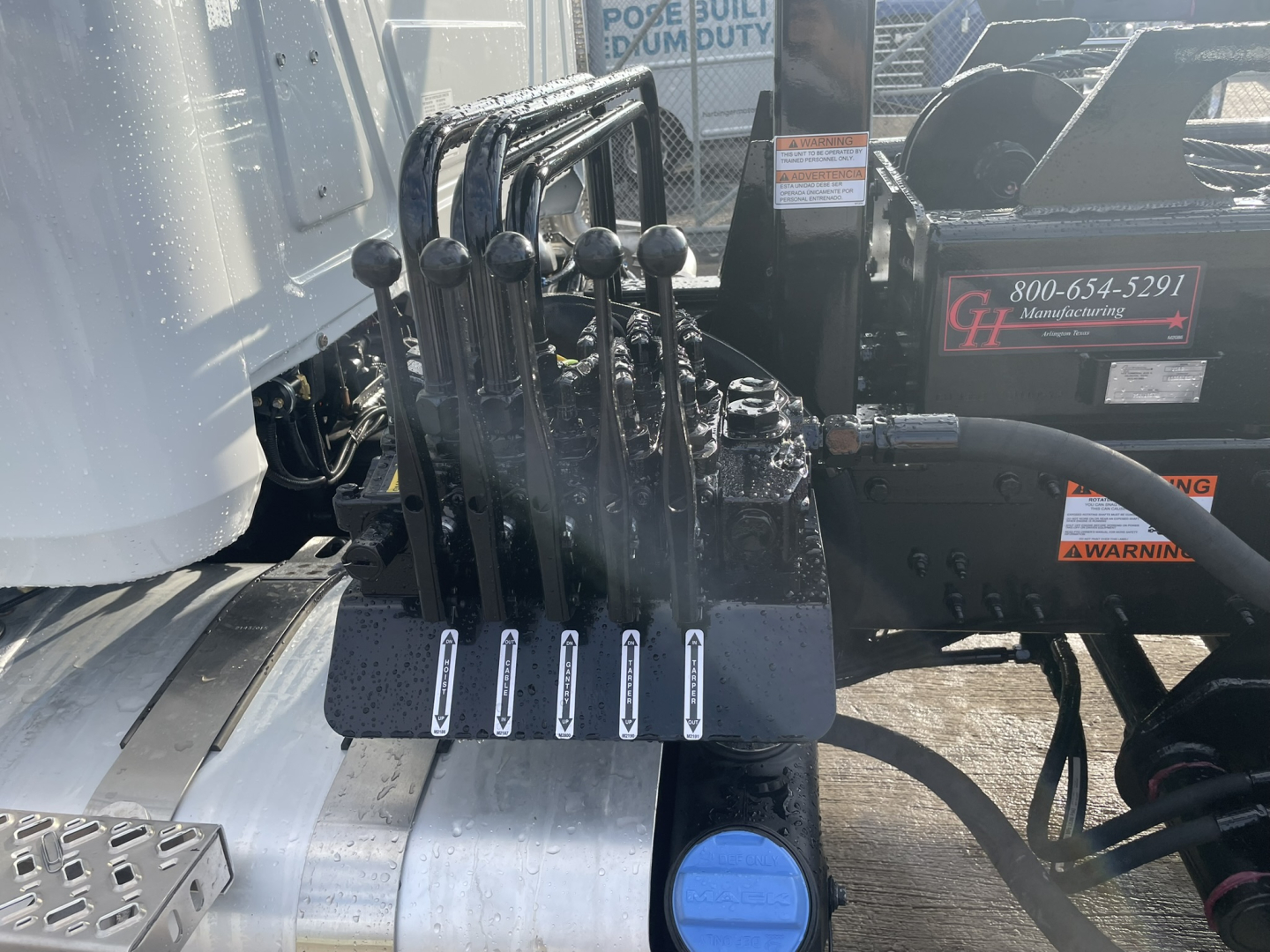 Levers and hydraulic control lever Assembly on Mack GR64B roll-off truck showing multiple black joystick levers and hydraulic connections.