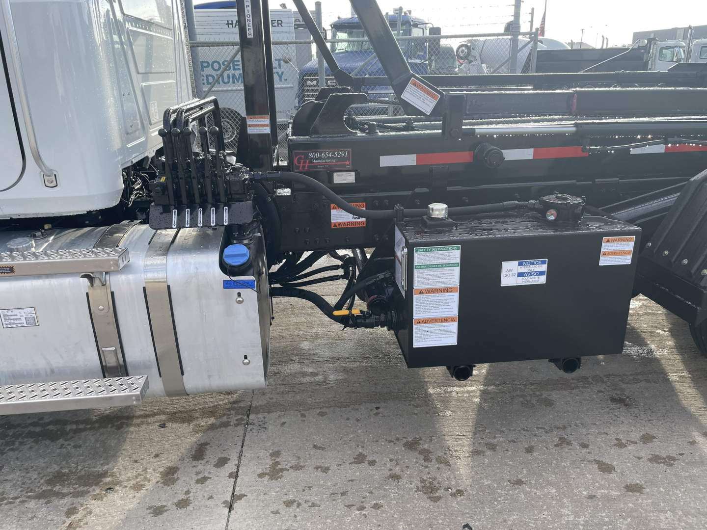 Mack GR64B roll-off truck chassis showing hydraulic pump area and auxiliary control box with labels.