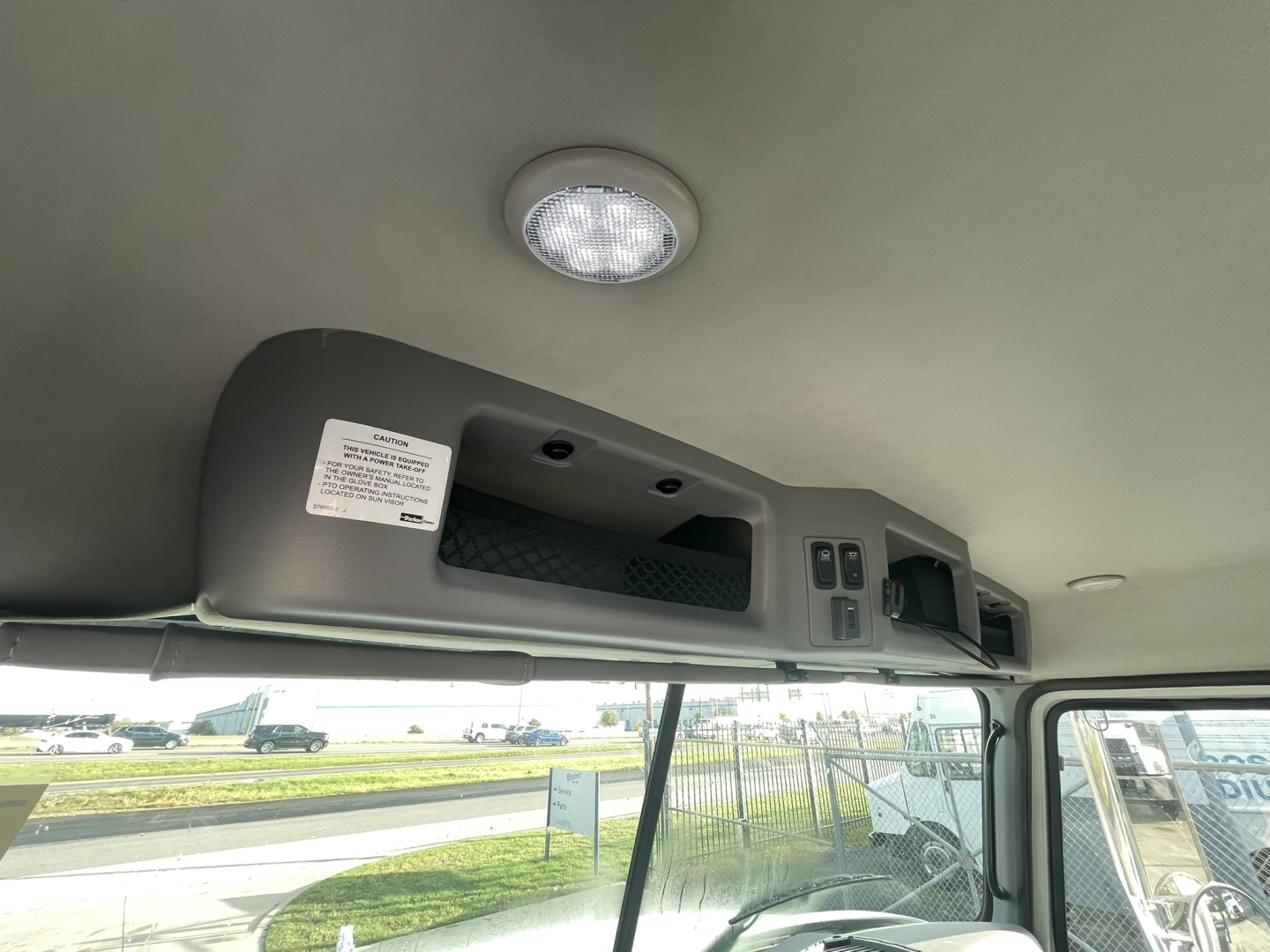 Mack GR64B truck interior overhead console with small label and circular dome light; dashboard area visible through windshield.