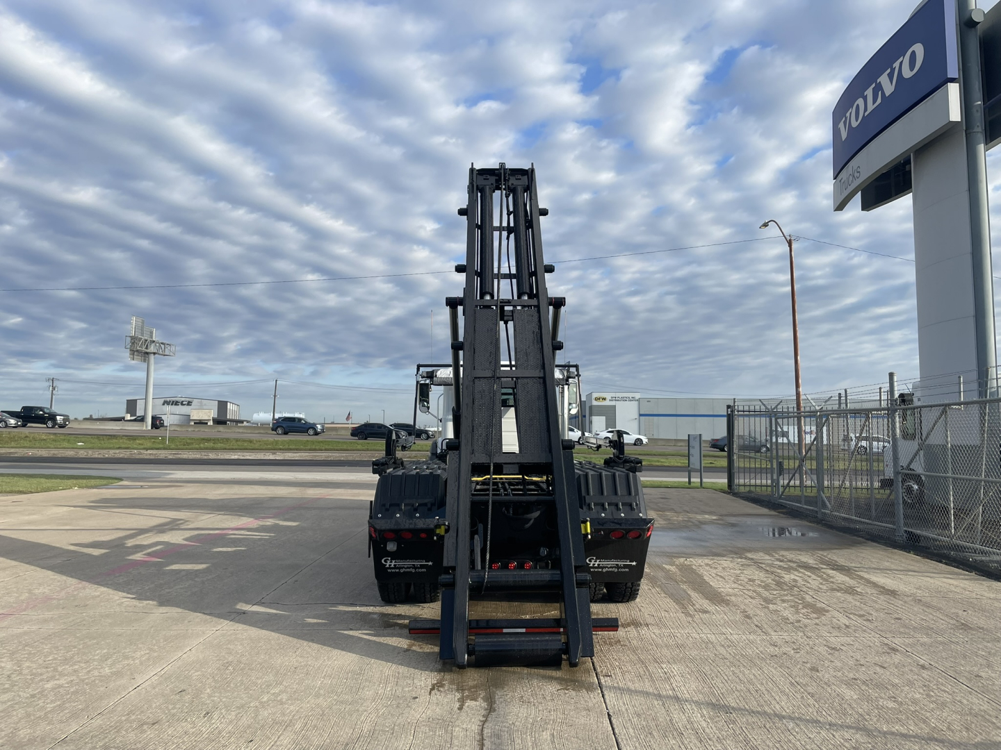 Mack GR64B roll-off truck viewed from rear with hydraulic loading arm in stowed position at a dealership lot.