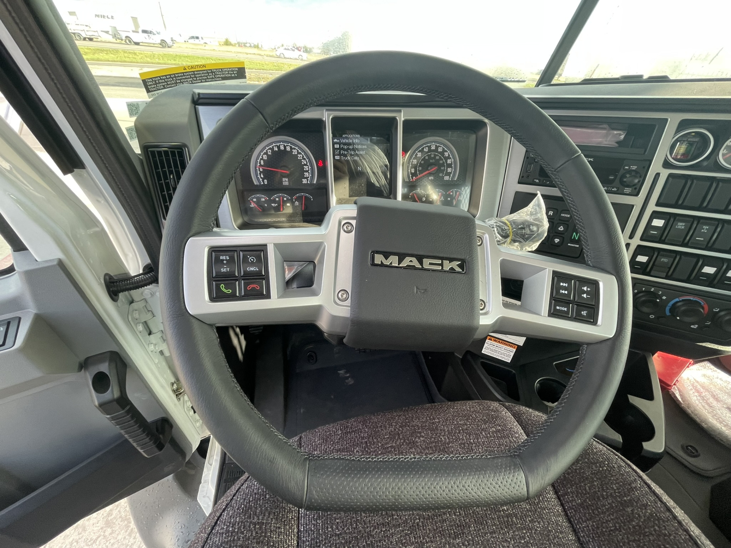 Dashboard and steering wheel of a Mack GR64B truck cab showing the Mack logo on the center of the steering wheel, gauge cluster, and control panels.