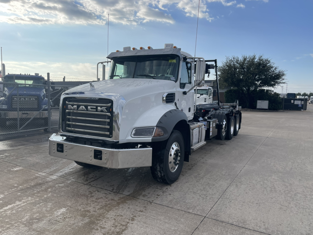 White Mack GR64B rolloff truck showing front grille with MACK letters and chrome bumper, daytime outdoor lot, multiple axles visible