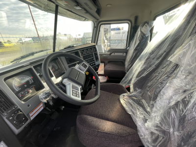 Cab interior of a new 2026 Mack GR64B rolloff truck showing steering wheel, dashboard gauges, and plastic-covered seats.