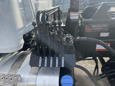 Levers and hydraulic control lever Assembly on Mack GR64B roll-off truck showing multiple black joystick levers and hydraulic connections.