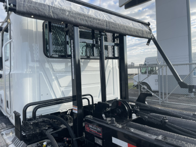Truck cab side of 2026 Mack GR64B roll-off with protective grille and hydraulic components visible near the chassis.