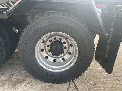 Wheel and tire of a Mack GR64B truck showing steel wheel with lug holes and heavy tread tire, part of a rolloff truck chassis.