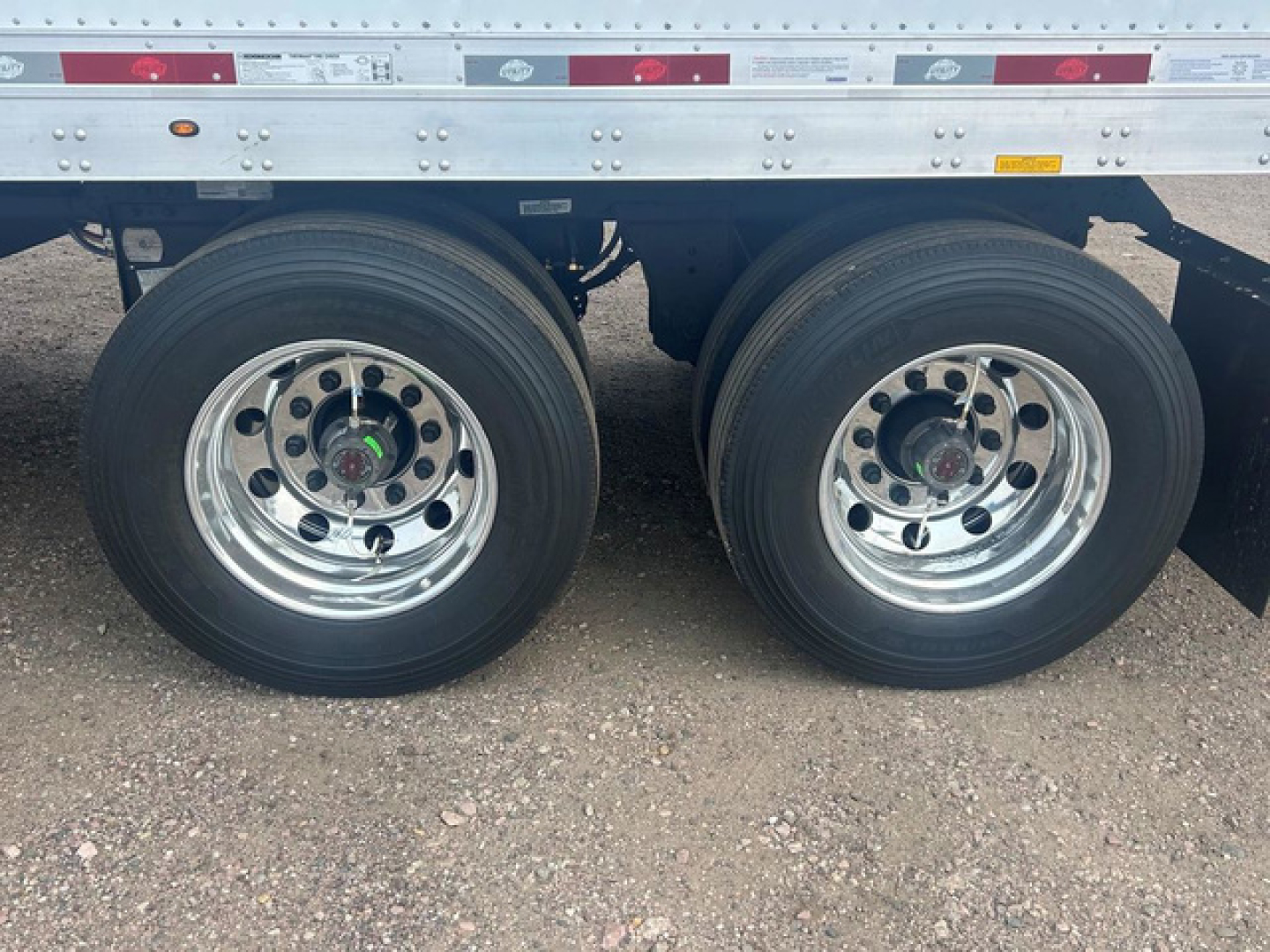Dual rear trailer wheels with polished chrome rims and black tires under a silver trailer side rail.