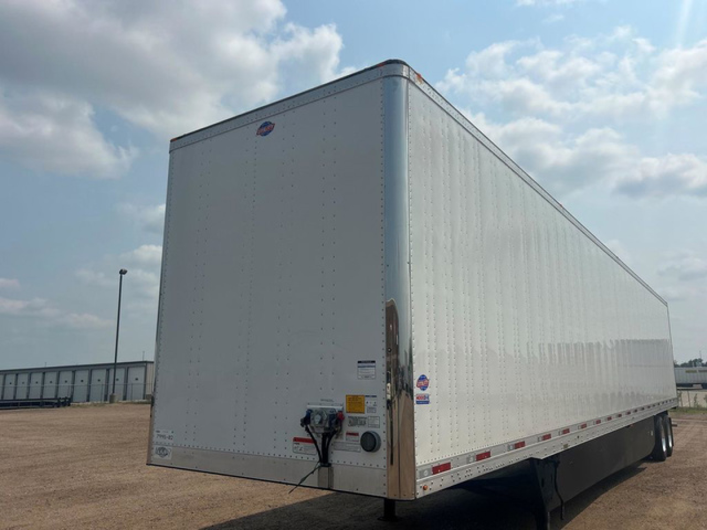 Trailer side and rear corner showing large white utility trailer with reflective tape and hitch, no visible branding details.
