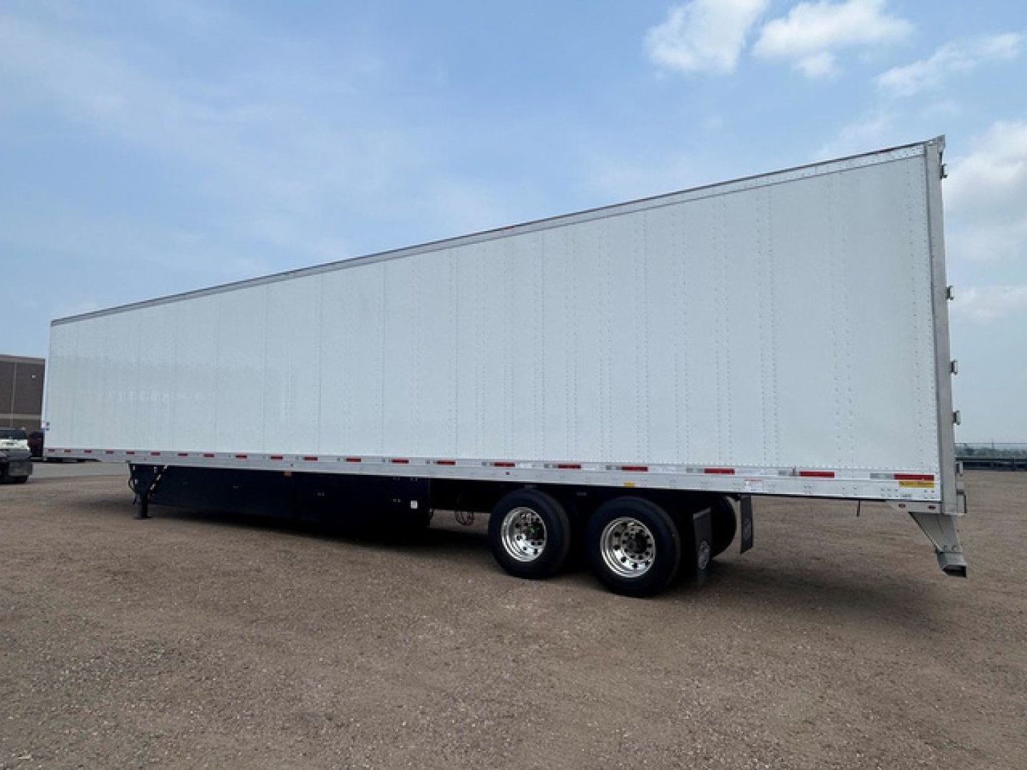 Trailer side view showing a long white utility trailer with dual rear axles and reflective safety rails.
