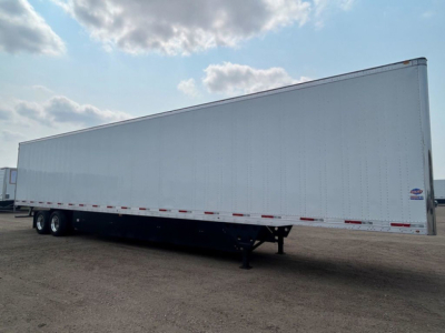 Trailer in a parking lot showing a long white box-style utility trailer with dual rear axles and a front hitch, no visible branding.