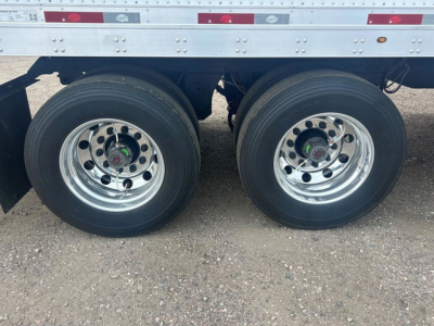 Trailer axle pair showing dual rear wheels on a Utility Dx trailer in new condition. Rust-free chrome rims with black tires, undercarriage and reflective tape visible.