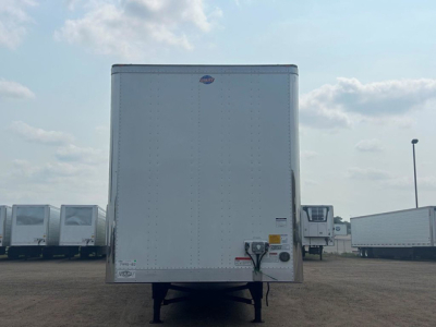 Rear view of a white Utility trailer with a numbered VIN label and hitch, showing a stub axle and rear doors, in a dealership lot.