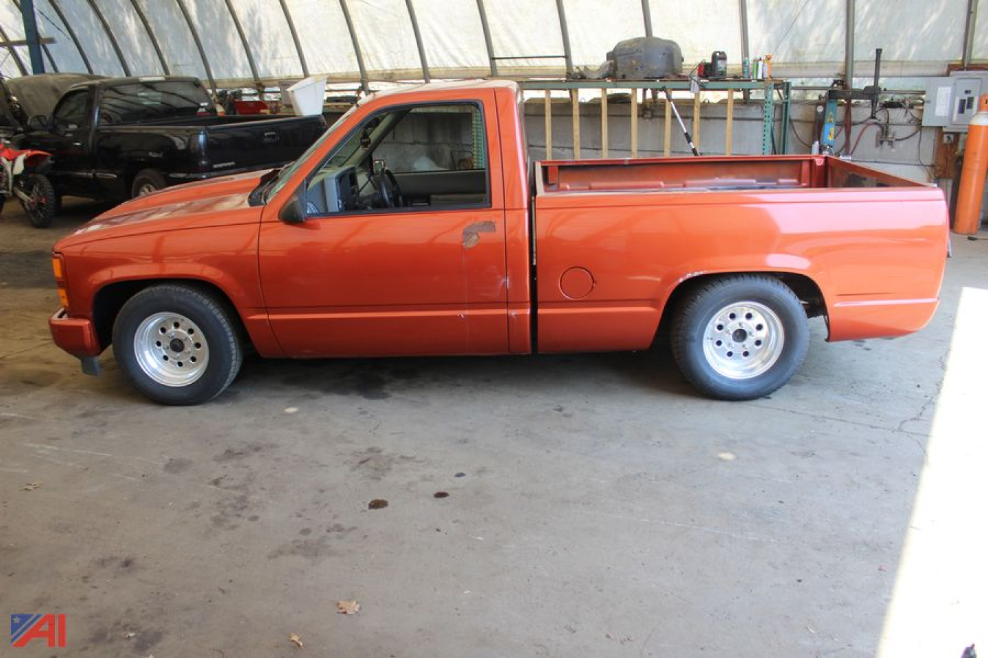 Chevrolet pickup truck side view showing orange 1992 C/K 1500 series with long bed in a covered area.
