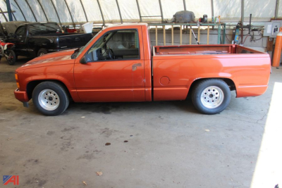 Chevrolet pickup truck side view showing orange 1992 C/K 1500 series with long bed in a covered area.