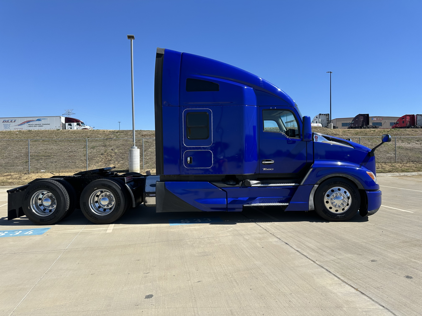 Kenworth T680 sleeper cab tractor in blue, side view showing side windows, door, and fuel tanks, street parking lot.