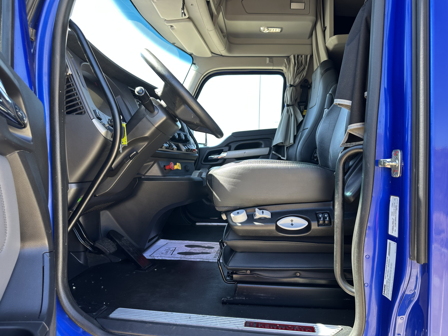 Kenworth T680 truck cab interior with driver seat controls, steering wheel, and dashboard visible from open door.