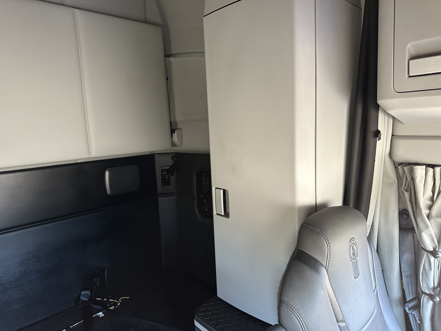 Kenworth T680 sleeper cab interior showing vertical cabinet and doorway area with light gray panels.