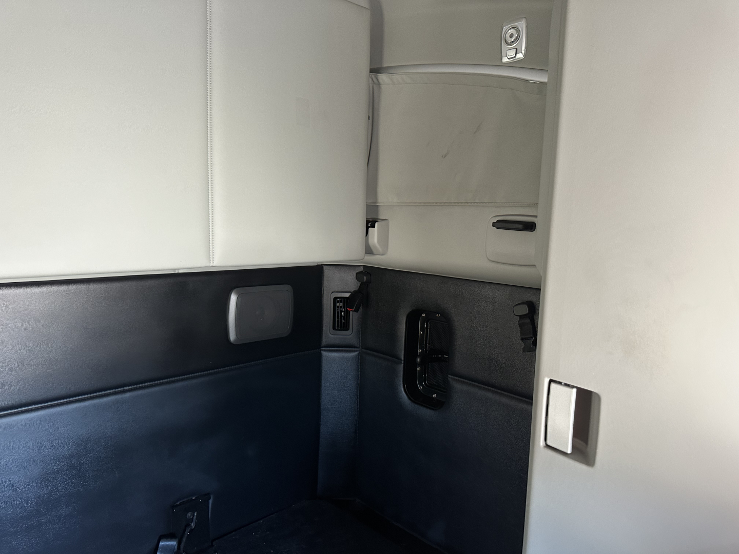 Kenworth T680 sleeper cab interior showing side wall with storage pocket and window, light gray upper panel, dark lower panel, and door trim.