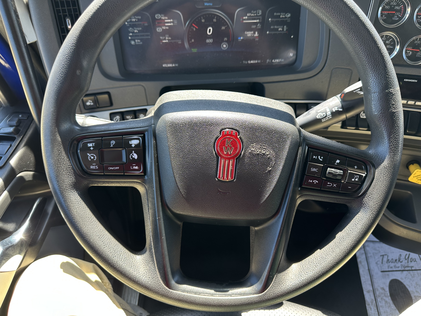 Kenworth T680 steering wheel and dashboard with instrument gauges visible, including steering wheel controls on both sides.