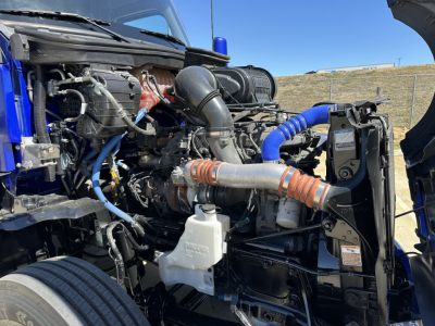 Kenworth T680 engine bay showing coolant reservoir and blue silicone hoses with exposed engine components.