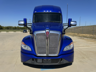 Kenworth T680 front view showing blue sleeper cab, chrome grille, and badge centered on grille.