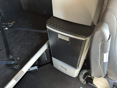 Kenworth T680 interior view showing overhead cabinet and center console with a small storage drawer and cubby; portion of seat and floor visible.