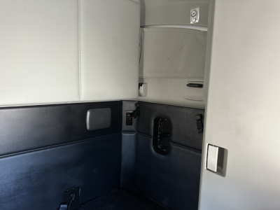 Kenworth T680 sleeper cab interior showing side wall with storage pocket and window, light gray upper panel, dark lower panel, and door trim.