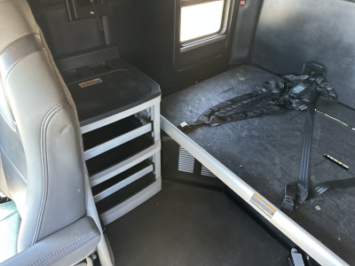 Kenworth T680 interior view showing sleeper area with seat, storage drawers, and seat belt harness.