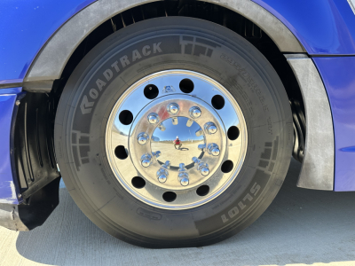 Truck wheel and tire on blue Kenworth T680 showing Load Trail tire with chrome hubcap and lug nuts