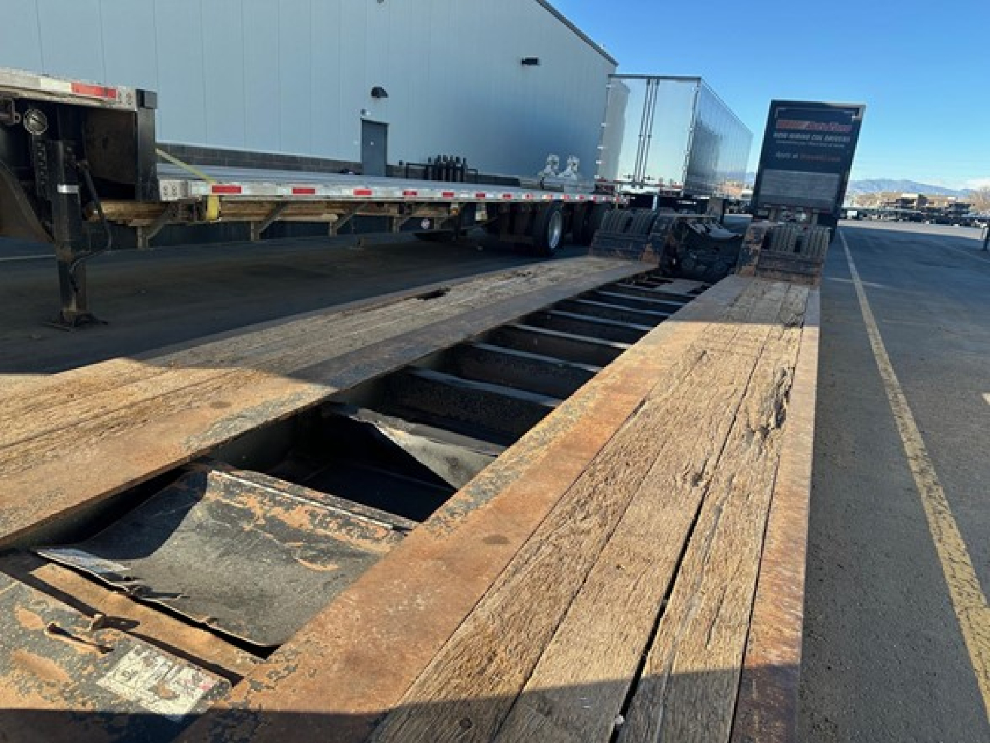 Trailer bed with wooden planks and cutouts showing a Fontaine 55 LCC lowboy trailer (industrial lot)