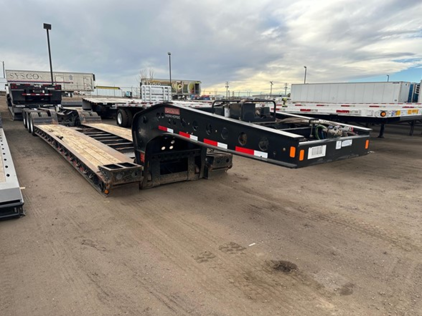 Lowboy trailer frame showing Fontaine 55 Lcc style gooseneck and deck with exposed steel structure and parking lot background.