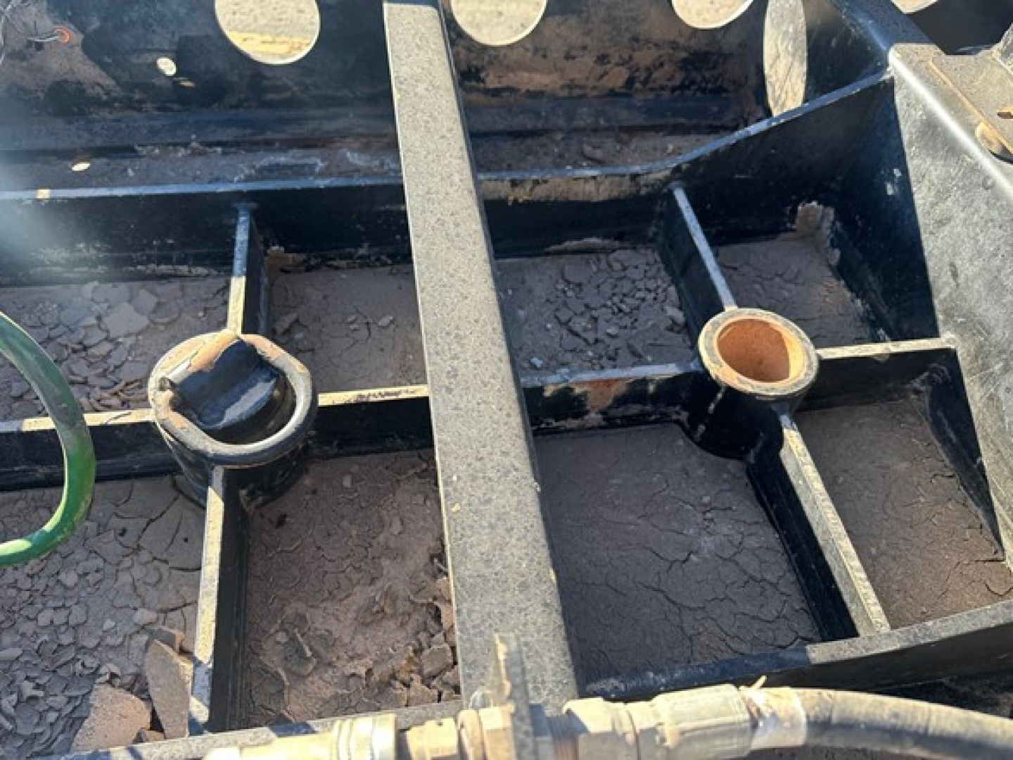 Trailer frame close-up showing a black steel subframe with circular mounting holes and a central I-beam; visible surface rust and dirt present.