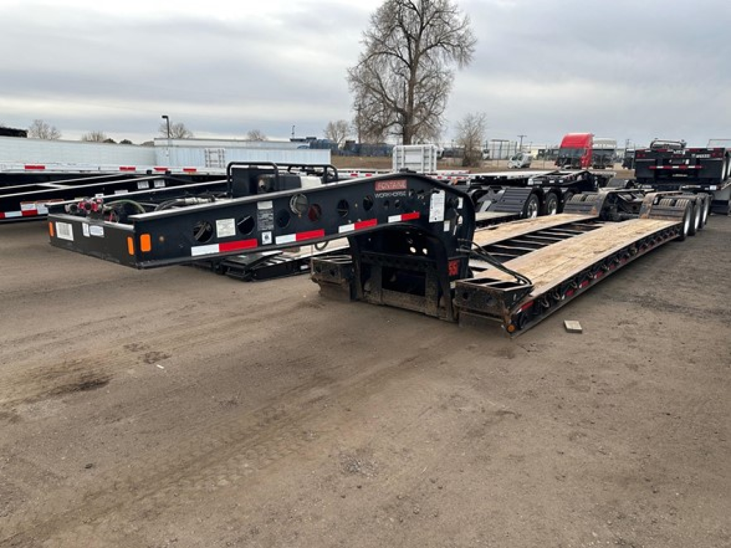 Trailer lowboy showing Steel frame, multiple axles, and loading ramps with visible branding and reflective tape.