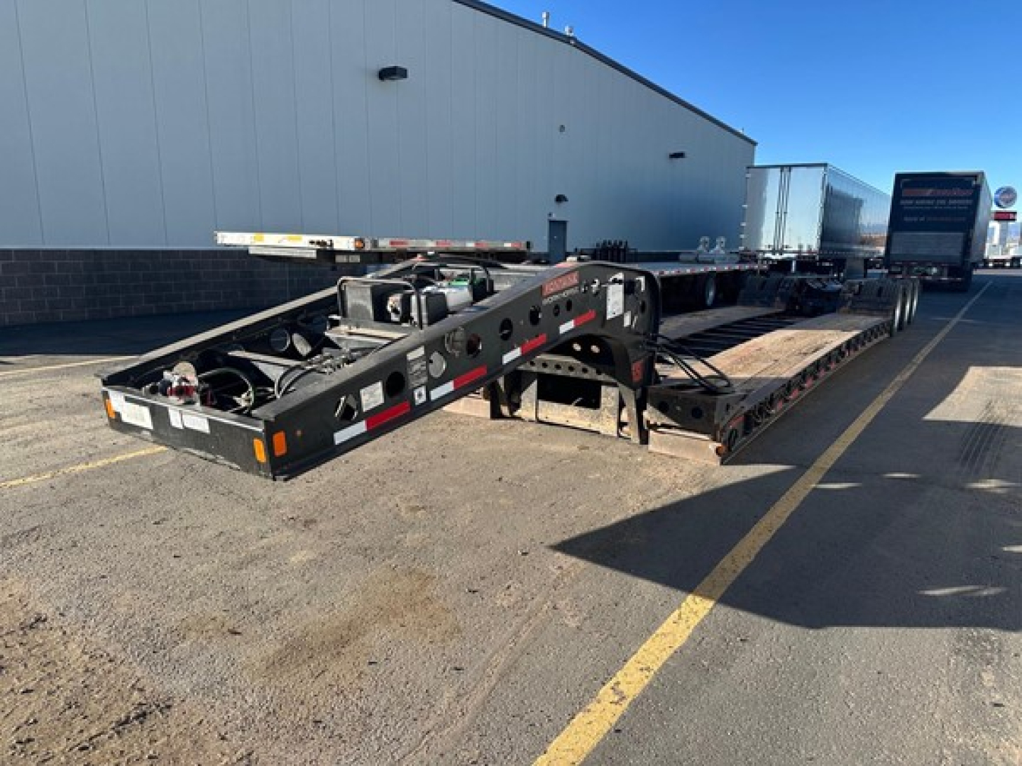 Trailer chassis and lowboy with extended gooseneck showing black steel frame, deck rails, and support legs.