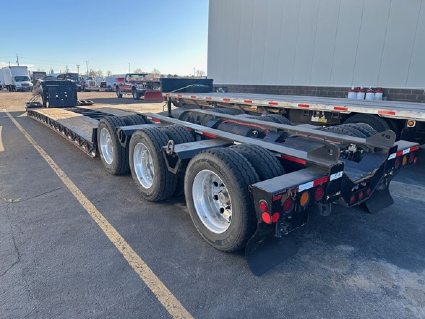 Lowboy trailer with multiple axles showing rear and side view, Fontaine 55 LCC trailer, metal deck, black frame, silver wheels, hubcaps, and reflective tape.