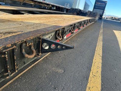 Flatbed trailer tail showing edge with hooks and metal framework, long lowboy trailer in a loading yard.