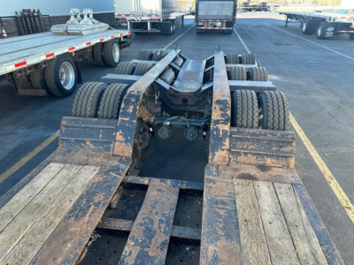 Lowboy trailer chassis showing wear and multiple axles with dual rear wheels; brown dirt on frame and wooden deck; Fontaine 55 LCC trailer indicated by context.