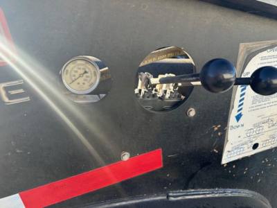 Trailer dashboard with gauge and control levers on black panel; red strip decal; circular gauge visible; labels and instruction sheet in view.