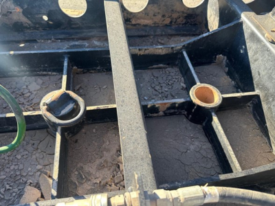 Trailer frame close-up showing a black steel subframe with circular mounting holes and a central I-beam; visible surface rust and dirt present.