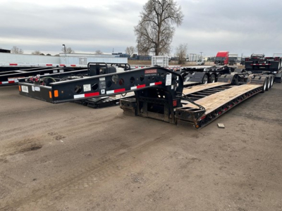 Trailer lowboy showing Steel frame, multiple axles, and loading ramps with visible branding and reflective tape.