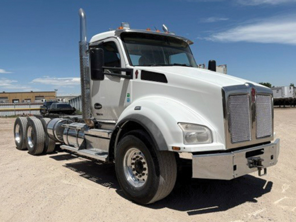 Kenworth T880 conventional daycab truck in side-front view showing large chrome grille and dual rear axles with chrome fuel tanks.