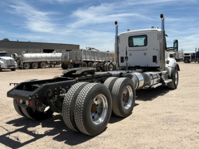 Kenworth T-880 tractor cab in a yard showing rear chassis and dual rear axles with fuel tanks and exhaust stacks.