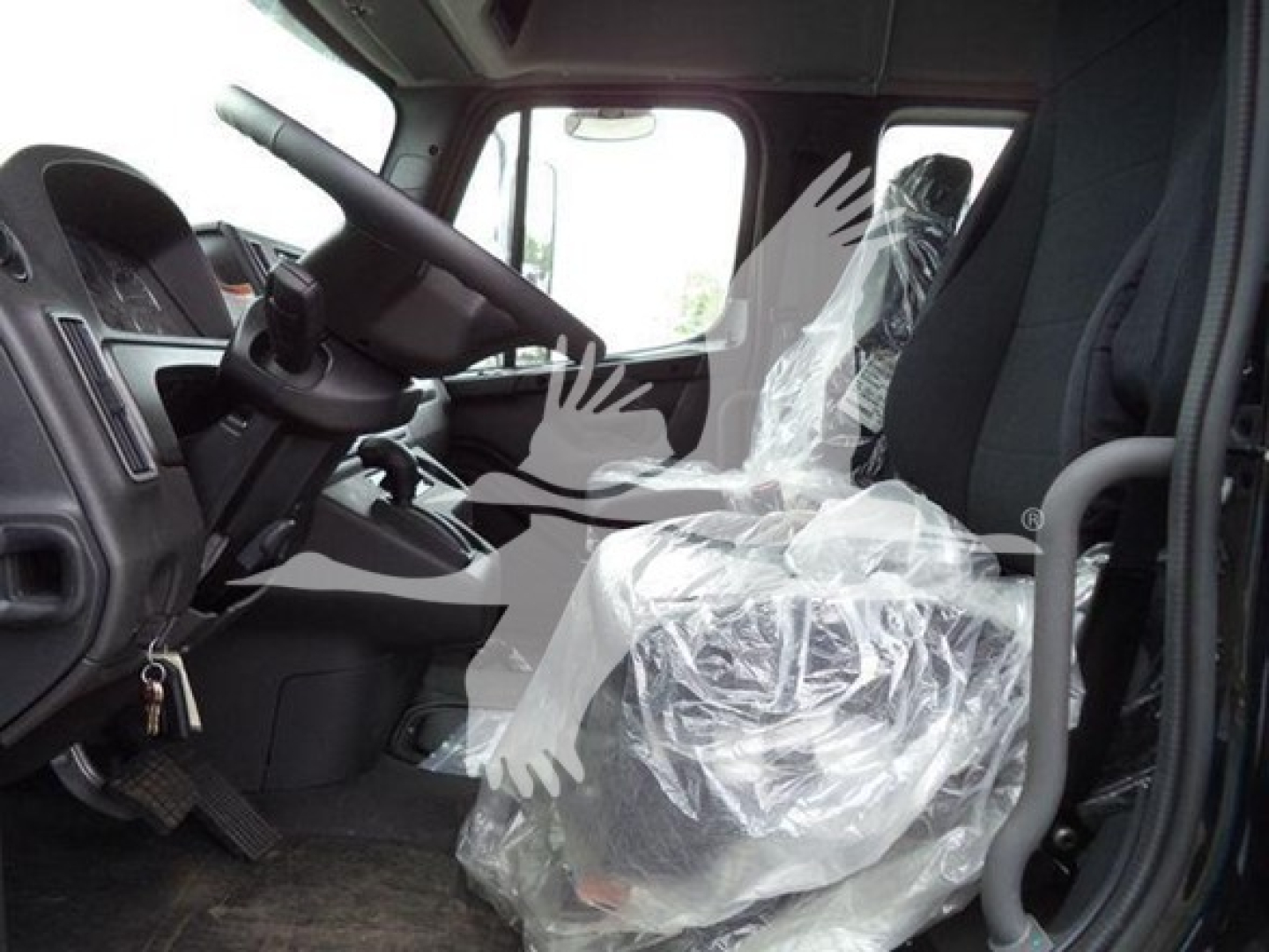 Truck cab interior with steering wheel, side door, and driver seat covered in plastic; visible pedals and ignition area.
