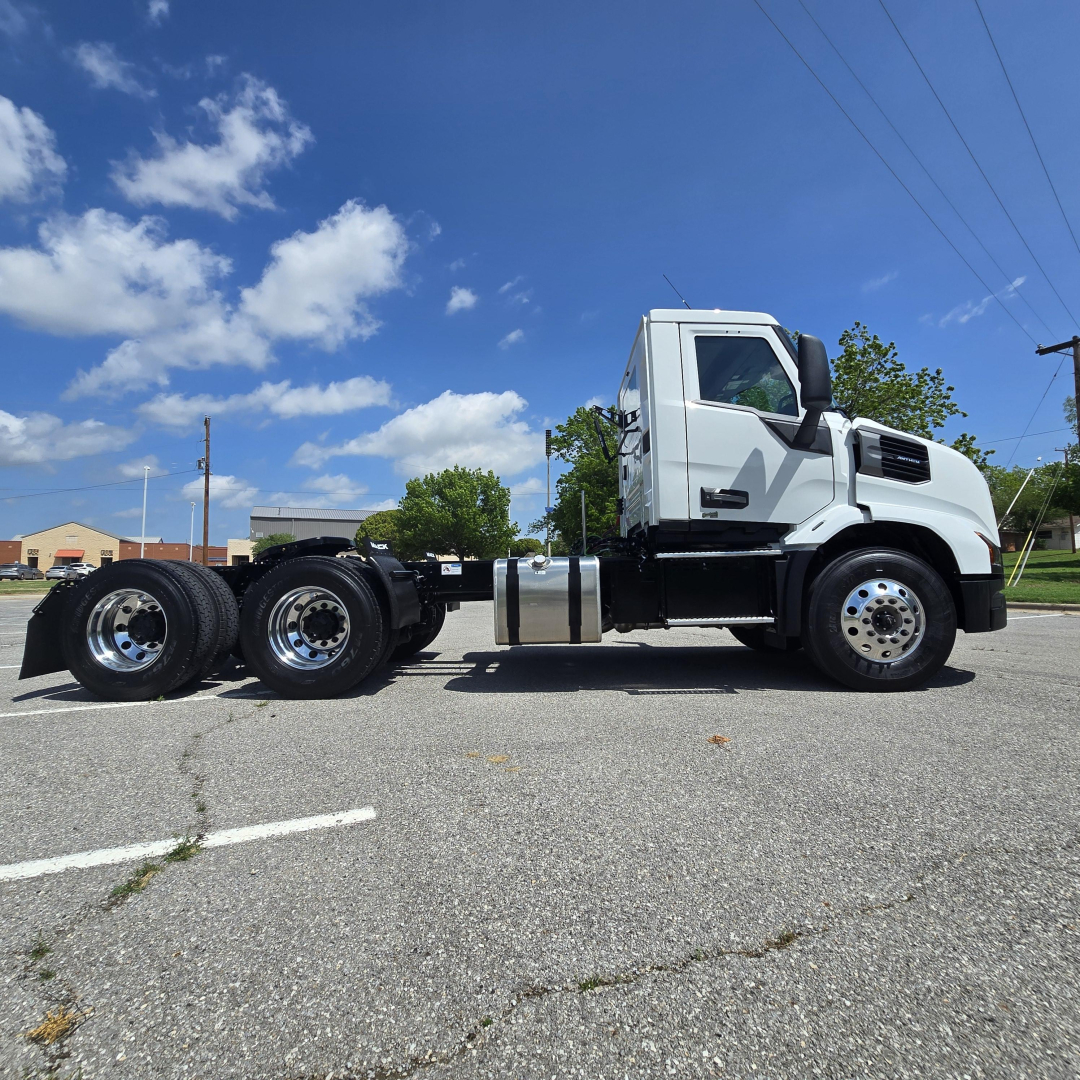 Truck chassis and cab of a 2027 Mack AN64T on concrete lot, side view showing front tires, cab, and rear axle.