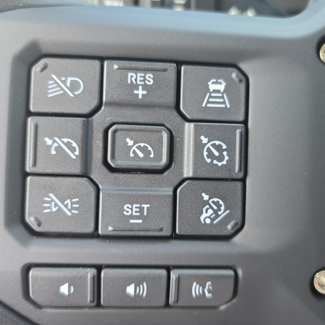 Dashboard steering wheel controls showing cruise control and speed limiter buttons on Mack AN64T truck instrument cluster.